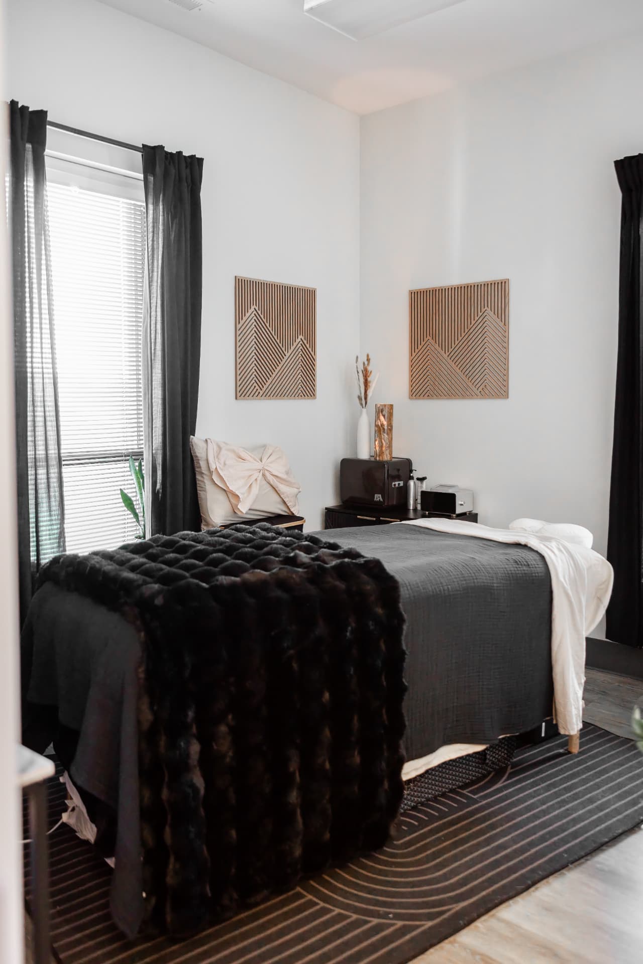 A serene Restora treatment room with dark linens, textured pillows, wood wall art, and soft natural light