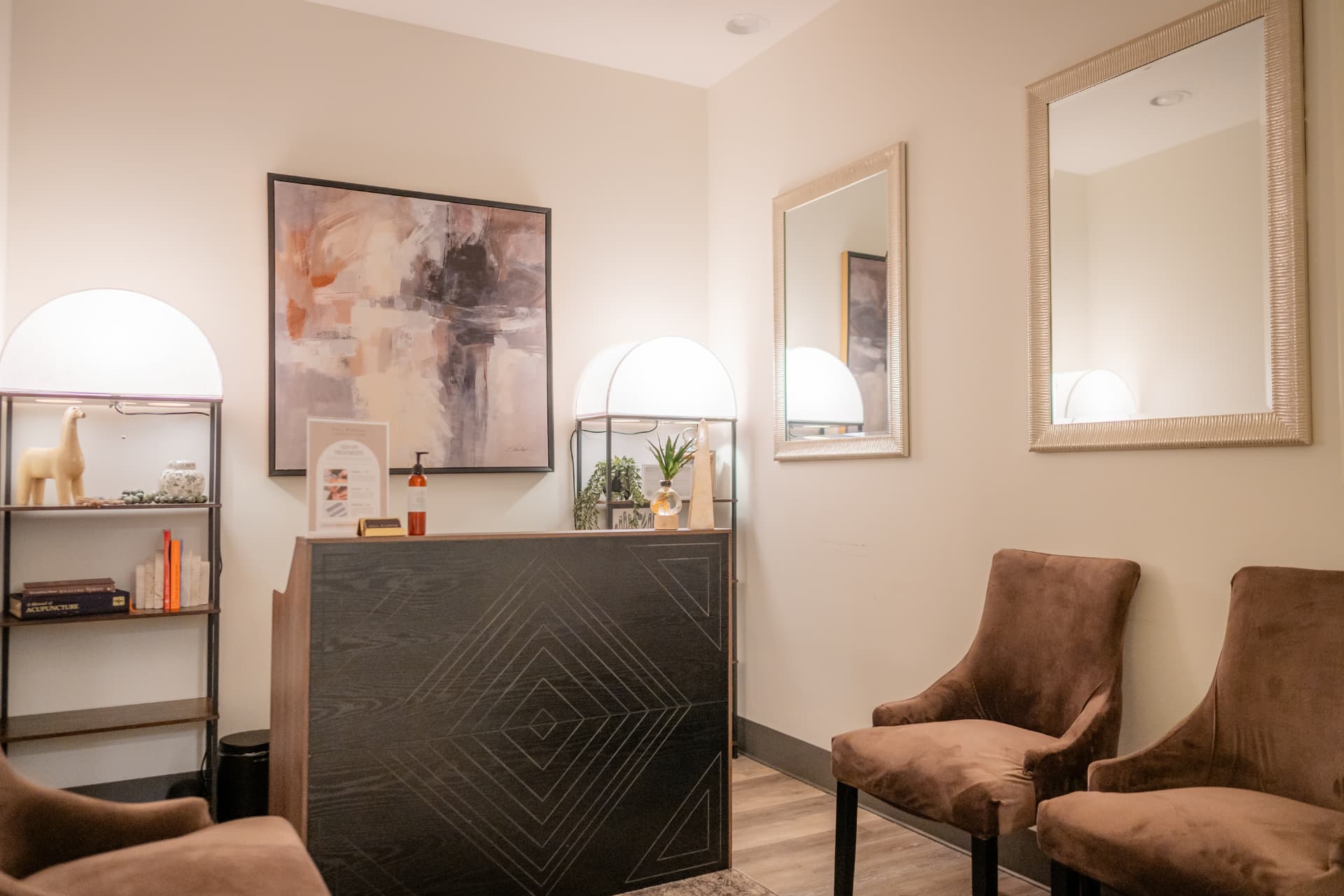 The warm reception area at Restora with a dark patterned desk, mirrors, abstract art, lamps, and upholstered chairs